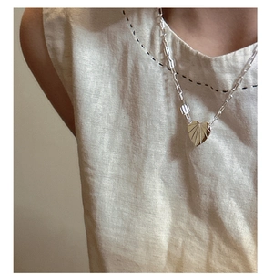 Gros plan d'un pendentif cœur argenté avec texture soleil sur une chaîne à maillons longs