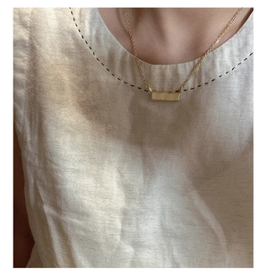 Primo piano della collana con pendente a barra dorata minimalista con finitura spazzolata