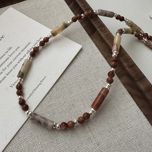 S925 silver necklace with brown stone cylinders and sand gold beads on linen fabric