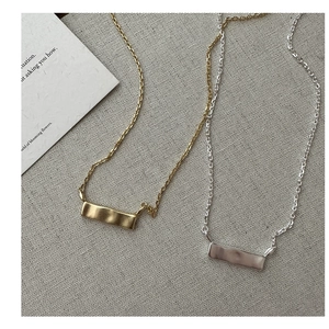 Dettaglio dei ciondoli quadrati irregolari opachi in oro e argento su un tessuto grigio
