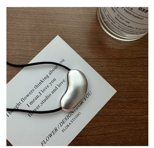 Detailed close-up of matte silver bean-shaped pendant with fine brushed metal texture