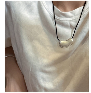Macro shot of an irregular silver bean pendant on a minimalist black cord necklace