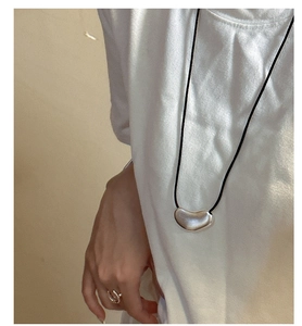 Detail of matte silver bean pendant necklace and adjustable ring on a female model