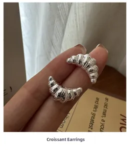 Close-up of silver croissant earrings showing intricate layered textures and polished finish