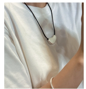 Minimalist silver heart pendant with black cord on model wearing a white t-shirt