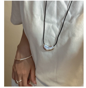 Close-up of minimalist silver bean pendant necklace and matching sleek open cuff bracelet