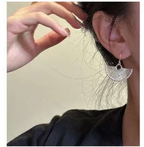 Detail of silver fan-shaped drop earrings with textured lines and a dark gemstone bead