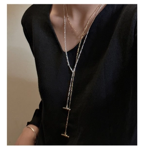 Detail of layered gold and silver Figaro chains with T-bar pendants on black knit
