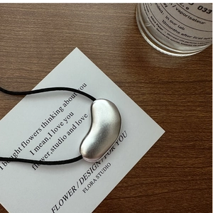 Macro detail of a silver matte bean pendant on a black cord over minimalist text card
