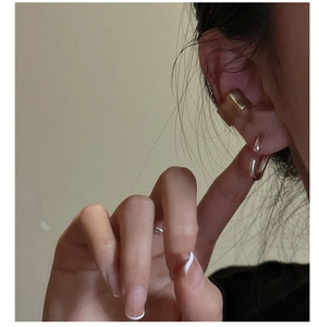 Detail of minimalist textured gold ear cuff and silver ring on person with sleek design