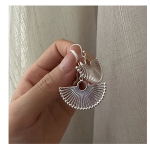 Detailed close-up of a silver fan-shaped earring with radial stripes and beaded edges