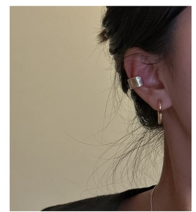 Close-up of minimalist silver textured ear cuff and gold hoop earring worn by a model