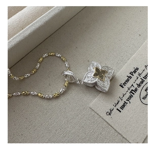 Macro view of two-tone S925 silver four-leaf clover pendant with intricate floral engravings