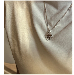 Gros plan d'un collier cœur en argent S925 avec zircon porté sur un pull en maille beige