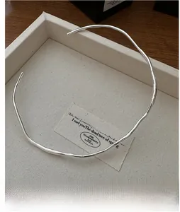 Detail of irregular silver liquid-metal collar necklace on beige textured display tray