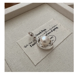 Close-up of a silver oval pearl pendant on a soft beige fabric background for jewelry