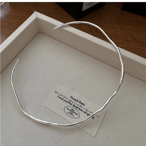Macro shot of minimalist silver wavy choker collar on a textured jewelry display tray