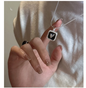 Detail of S925 silver heart necklace with black enamel inlay and woven chain on knits