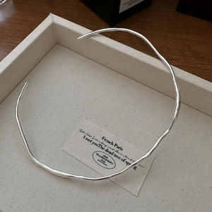Minimalist S925 silver wave liquid choker necklace on textured jewelry display tray