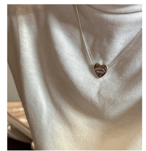 Detailed view of silver heart pendant engraved with EXPECTATION FUTURE on white knitwear