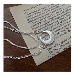 Macro detail of double-layer S925 silver crescent moon necklace on vintage paper