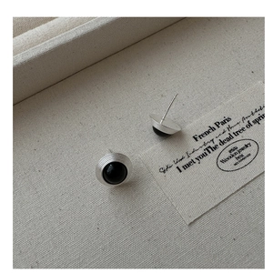 Détail de boucles d'oreilles en argent S925 mat avec perles noires sur plateau beige