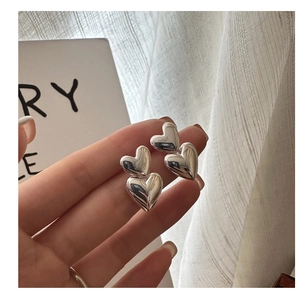 Close-up of dual heart sterling silver stud earrings with high-polish mirror finish