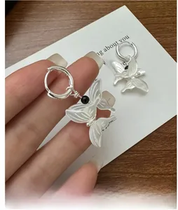 Macro detail of silver hoop earrings with white butterfly charms and black bead accents