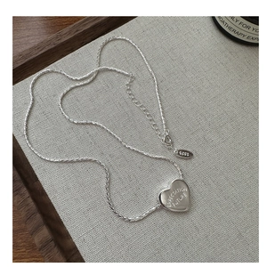 Macro detail of S925 sterling silver heart pendant with engraved text and chain texture