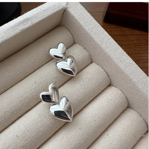 Macro shot of silver stacked double heart earrings on a soft beige velvet jewelry display