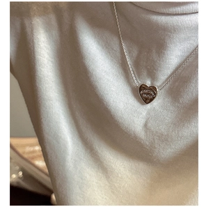 Detail of silver heart pendant with Expectation Future engraving on white sweater