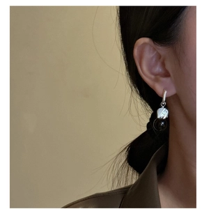 Detail of silver elephant earring with black onyx bead worn against a leather coat
