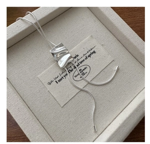 Macro shot of silver textured rectangular pendant on snake chain with vintage card