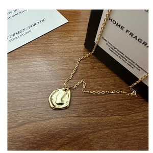 Détail d'un pendentif texturé doré minimaliste sur une chaîne posée sur du bois