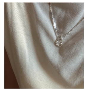 Close-up of minimalist S925 sterling silver hollow double heart pendant on knitted fabric