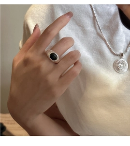 Detail of minimalist silver ring with black oval stone and sunburst coin necklace set