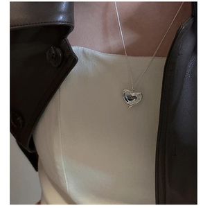 Close-up of irregular heart pendant on silver chain worn with a stylish leather jacket