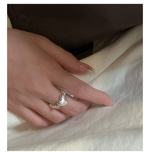 Détail d'une bague coeur en argent S925 avec anneau perlé portée au doigt sur tissu