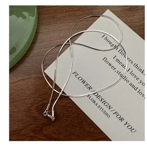 Detailed view of a delicate silver snake chain necklace on minimalist prop background