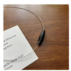 Detail shot of a sleek black spindle pendant on a delicate silver bead chain necklace