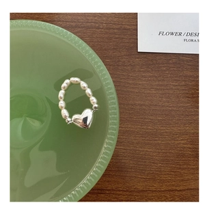 Vue détaillée d'une bague en perles avec pendentif cœur en argent sur un plateau en verre