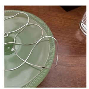 Detail of silver S925 snake bone chain on green ceramic plate with metallic reflection