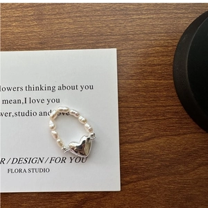 Détail de la bague en argent S925 avec breloque cœur et perles sur une carte sobre