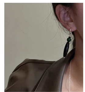 Close-up of long drop earrings with dark green beads and black oval stones on a model