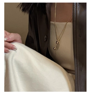 Close-up of golden ball pendant long chain necklace on model wearing brown leather jacket