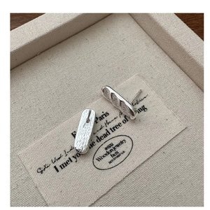 Macro detail of S925 sterling silver baguette-shaped stud earrings on a vintage paper
