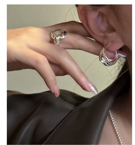 Close-up of chunky silver braided hoop earrings and wide ring on a female model