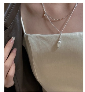 Detail of layered S925 silver necklace featuring a water drop gemstone and pearl charm
