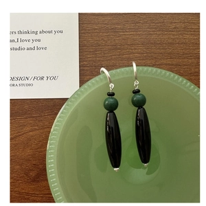 Detail of S925 silver long drop earrings with green and black agate beads on a dish
