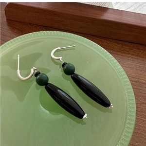 Macro detail of S925 silver earrings with green beads and black agate drops on glass tray